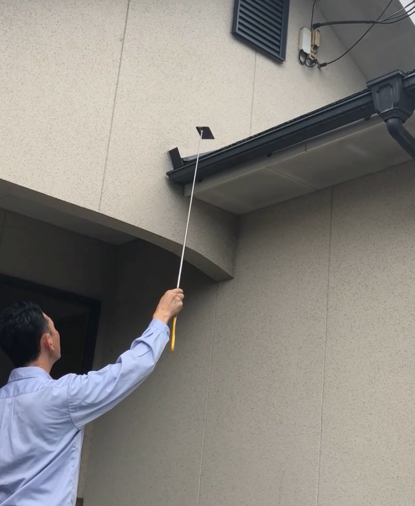 雨どい　棒付きミラーで詰まりを確認している